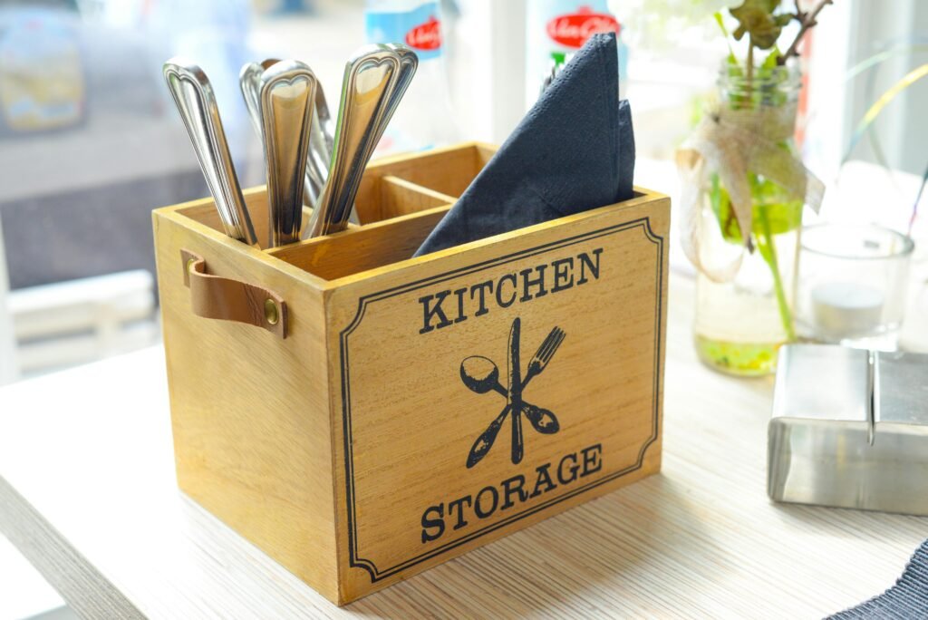 Close-up of a wooden kitchen storage box holding cutlery and napkins on a table setting.