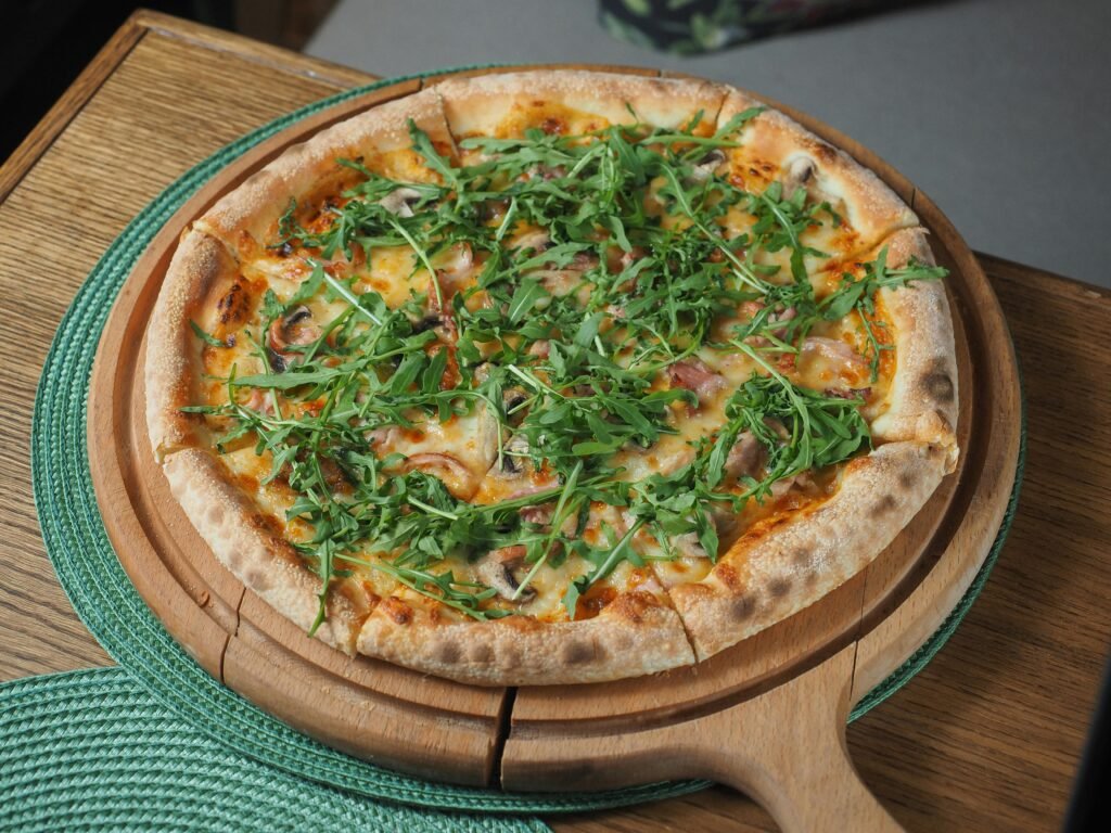 Freshly baked homemade pizza topped with arugula and cheese on a wooden board.