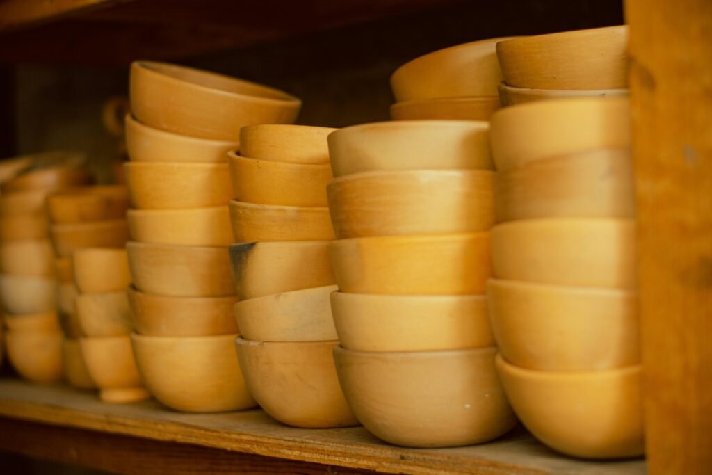 Home A collection of handcrafted wooden bowls neatly stacked on a rustic wooden shelf.