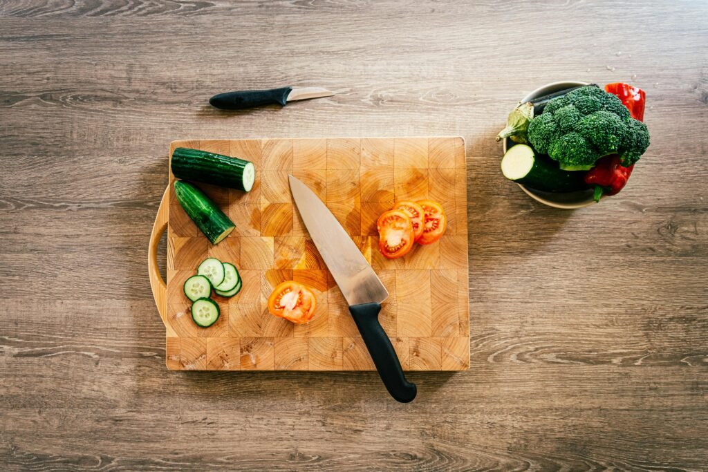 Wooden Products Exported from India Sliced cucumbers and tomatoes on a wooden cutting board with a knife.