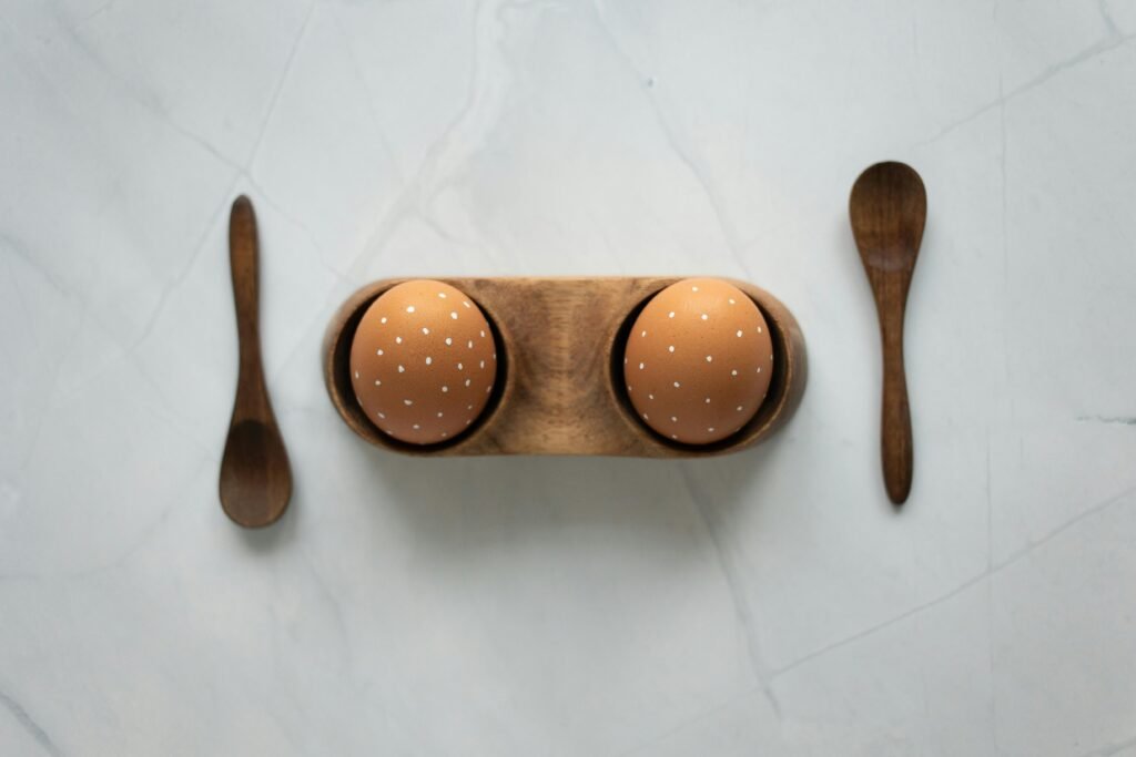 Top view of decorative Easter eggs with wooden spoons in a minimalist setup on a marble surface.